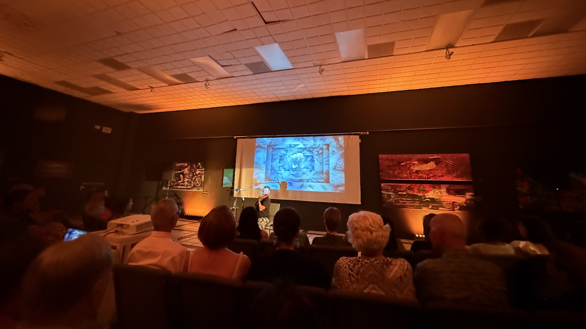 Close-up of Vic Renaudéau playing violin with blue abstract projection behind him at Cas di Cultura